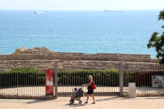 Una dona passant amb el carret d&#039;un nadó per davant de la reixa de l&#039;amfiteatre romà de Tarragona, tancat al públic de forma provisional