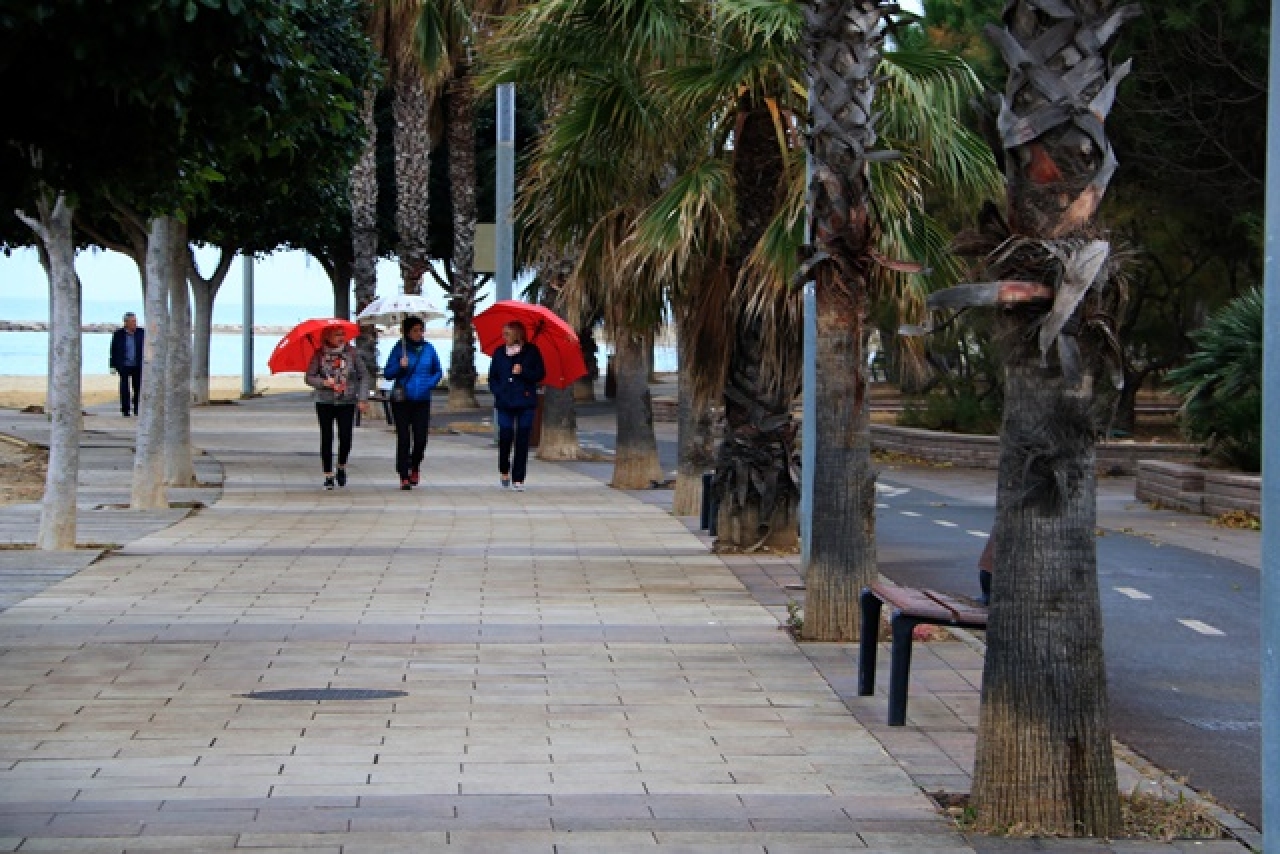 Tres dones passegen amb paraigües pel passeig Marítim de Cambrils, l&#039;últim dia del pont de la Puríssima