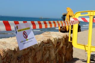 Un cartell informant que la platja d&#039;Altafulla restarà tancada durant nou hores, mentre una màquina arregla els desperfectes
