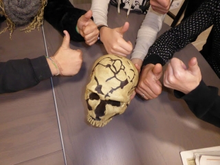 Imatge de mans de joves, amb el polze alçat, que resideixen en centres tutelats de Reus i Tarragona, amb un crani com a material divulgatiu que fan servir en sessions formatives de prehistòria