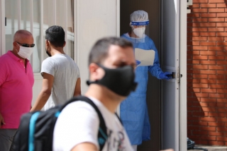 Una sanitària, amb una llista de pacients a les mans per fer-se la prova PCR, obrint la porta d&#039;un mòdul habilitat al CAP Sant Pere de Reus, mentre a fora hi ha gent esperant amb mascaretes