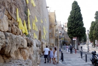 Llaços grocs penjats a la Muralla de Tarragona, amb turistes dirigint-se al portal del Roser, al fons, el passat 28 d&#039;agost