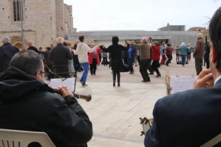 Diverses persones ballant sardana a Montblanc. En primer pla, d&#039;esquenes, dos músics de la cobla