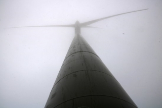 Imatge on es pot veure un aerogenerador des de la base, envoltat de boira, al parc eòlic de la Serra de Montargull, entre la Segarra i la Conca de Barberà