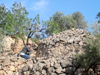 La investigadora Cèlia Mallafrè prenent mides d&#039;una construcció de pedra en sec