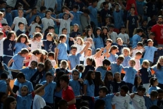Alumnes tarragonins, agafats i donant-se les mans, durant la cantada conjunta de la cançó oficial dels Jocs Mediterranis, en un acte multitudinari a la Tarraco Arena Plaça